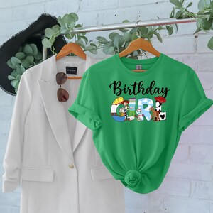 May include: Green t-shirt with a black "Birthday Girl" text and a graphic of Toy Story characters. The characters are arranged to spell out "GIRL".