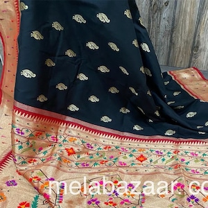 May include: A black and gold saree with a floral pattern and a red border. The saree has a gold and black pallu with a paisley design. The saree has a black tassel trim.