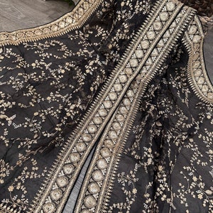 May include: A black sheer shawl with gold embroidery and sequins. The shawl has a floral pattern and a long, open front.