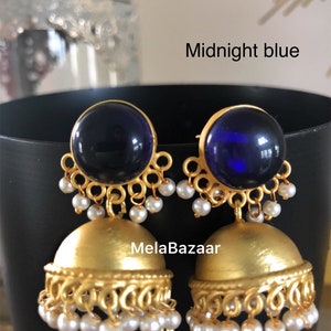 May include: A pair of midnight blue and gold-colored earrings. The earrings have a large, round, dark blue stone at the top, with a gold filigree design. The bottom portion is a gold bell shape with dangling white pearls. The text "Midnight blue" is visible.