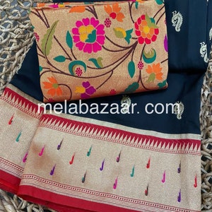 May include: A black saree with a gold and red border. The saree has a floral pattern and a paisley design. The saree is on a woven basket.