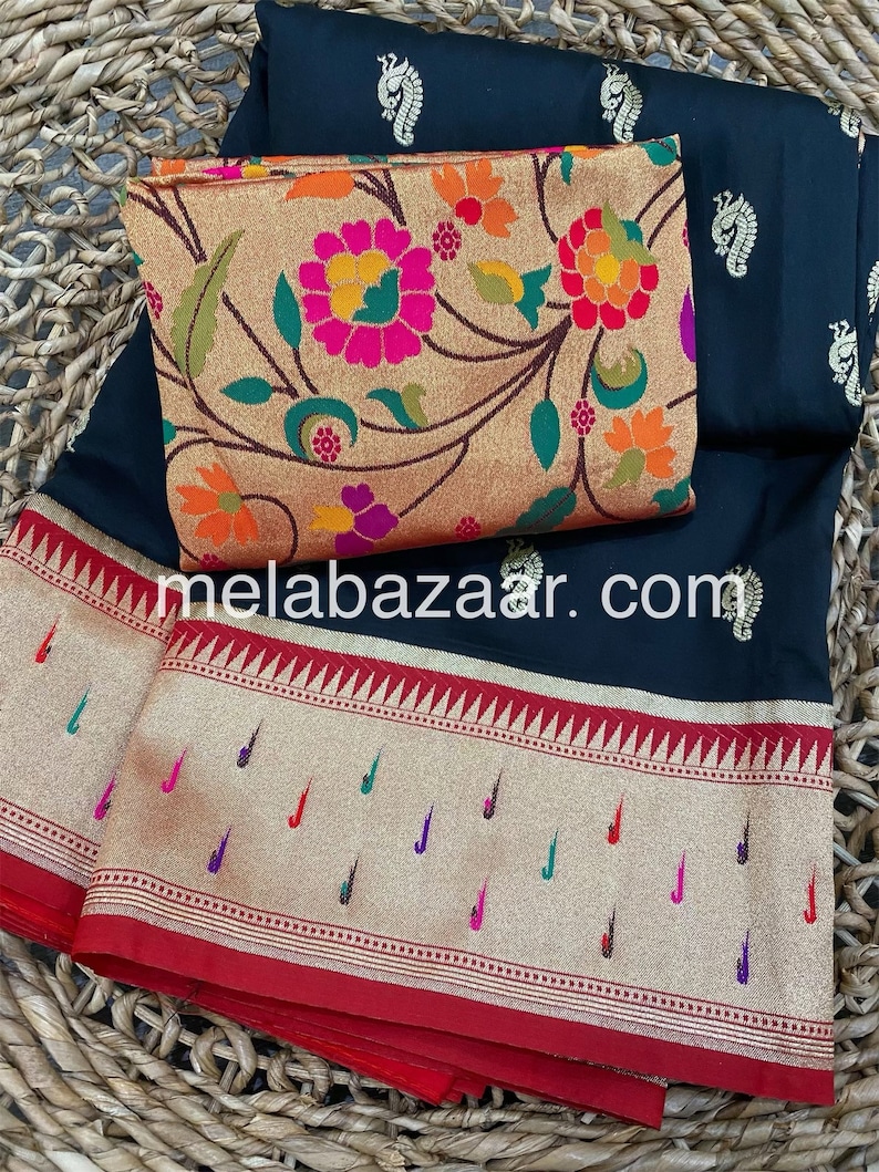 May include: A black saree with a gold and red border. The saree has a floral pattern and a paisley design. The saree is on a woven basket.