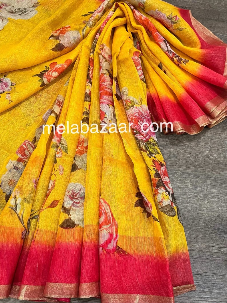 May include: A yellow linen saree with a floral print and a pink ombre effect at the bottom. The saree has a gold border.