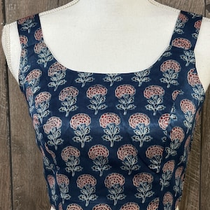 Puede incluir: Un top azul sin mangas con estampado floral con flores rosas y blancas. El top tiene un escote cuadrado.