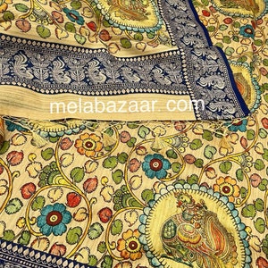 May include: A cream-colored fabric with a blue border and intricate floral and bird designs. The fabric features a repeating pattern of peacocks, flowers, and leaves in shades of blue, green, yellow, red, and orange. The fabric is woven with a fine texture and has a soft, luxurious feel.