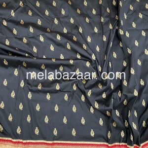 May include: Black silk saree with a gold paisley pattern and a red and gold border. The saree is folded and the border is visible. The text "melabazar.com" is printed on the saree.