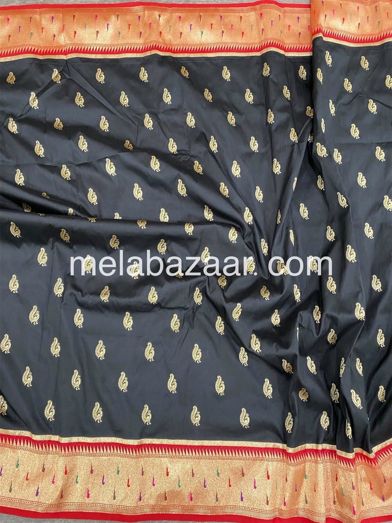 May include: Black silk saree with a gold paisley pattern and a red and gold border. The saree is folded and the border is visible. The text "melabazar.com" is printed on the saree.