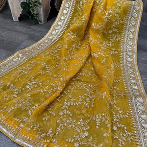 Puede incluir: Un pañuelo de gasa amarillo con un patrón floral bordado en plata y un borde de cuentas plateadas.