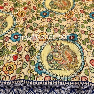 May include: A cream-colored fabric with a repeating pattern of peacocks, flowers, and leaves. The fabric has a blue and silver border with a paisley design.