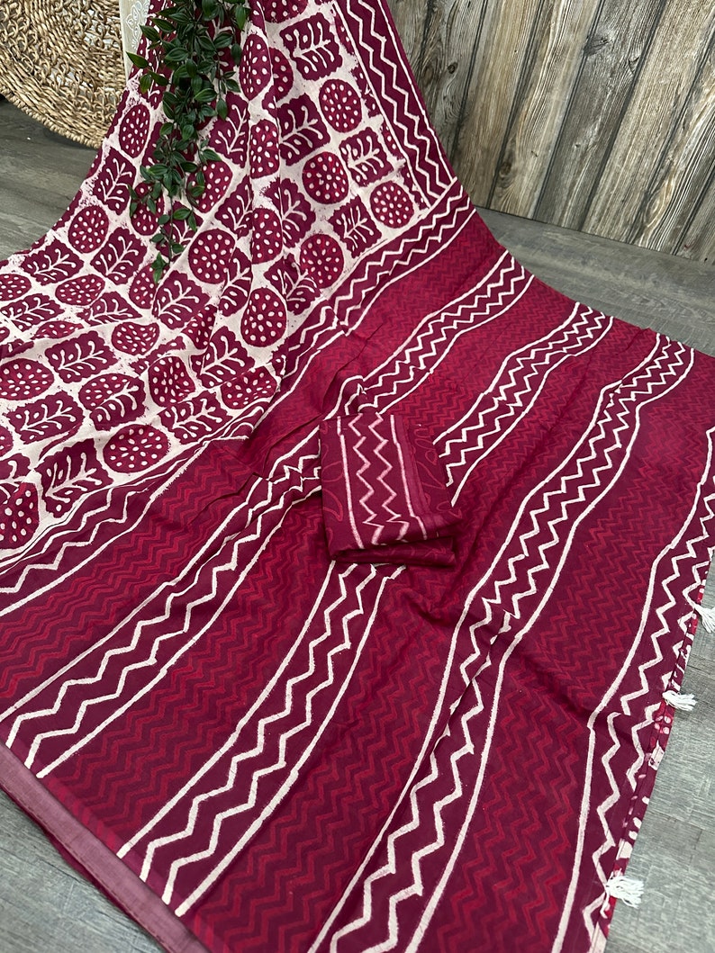 K&ouml;nnte beinhalten: Bordeaux-wei&szlig;es Textil mit sich wiederholendem Blatt- und geometrischem Muster. Der Stoff weist eine Kombination aus vertikalen Streifen und Zickzackmustern auf, mit einem passenden Stoffst&uuml;ck.