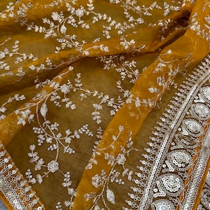 May include: A mustard yellow sheer fabric with a silver floral embroidery pattern. The fabric has a silver sequined border.