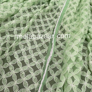 May include: A light green sheer fabric with white embroidered floral designs. The fabric has a delicate, airy feel and is perfect for creating garments or home decor.