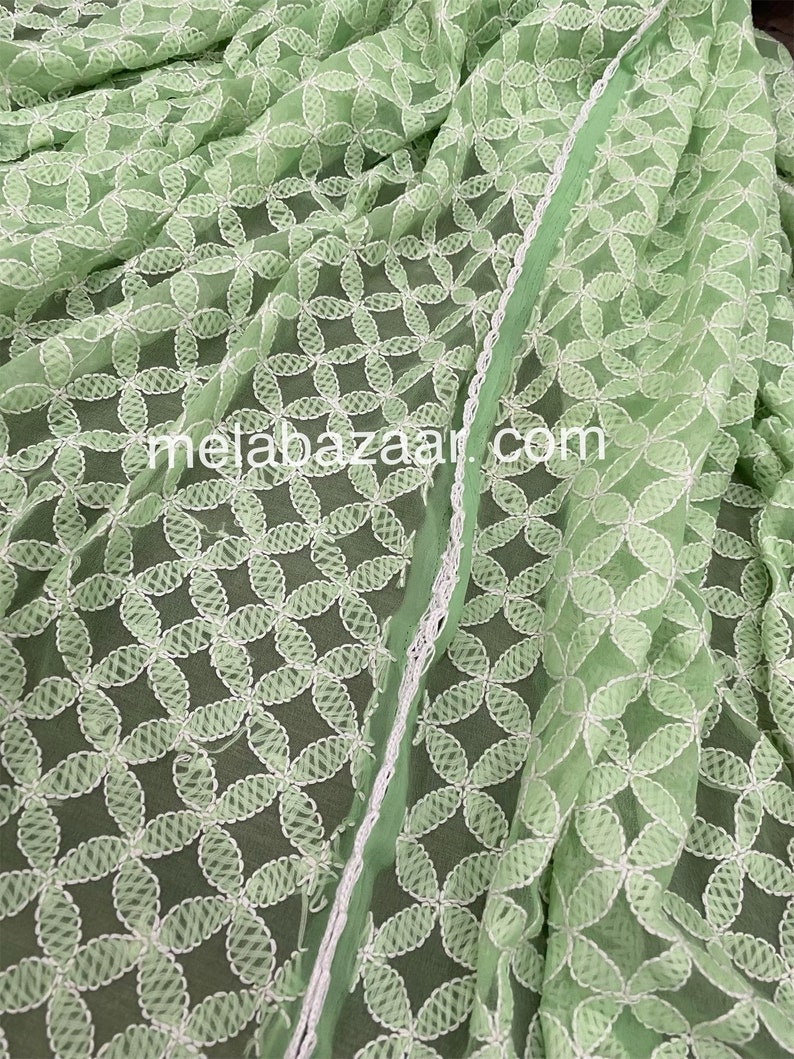 May include: A light green sheer fabric with white embroidered floral designs. The fabric has a delicate, airy feel and is perfect for creating garments or home decor.