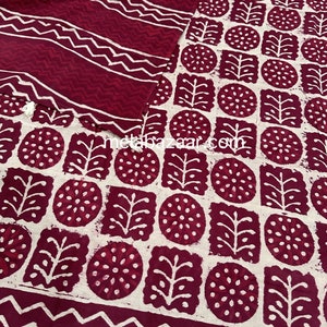 K&ouml;nnte beinhalten: Ein zweiteiliges Set mit einem bordeauxroten und wei&szlig;en geometrischen Muster. Der Stoff zeigt ein sich wiederholendes Design aus Kreisen, Quadraten und Blattformen. Das Set enth&auml;lt ein Oberteil und einen passenden Schal, beide mit wei&szlig;en Zickzack- und Streifenmustern.