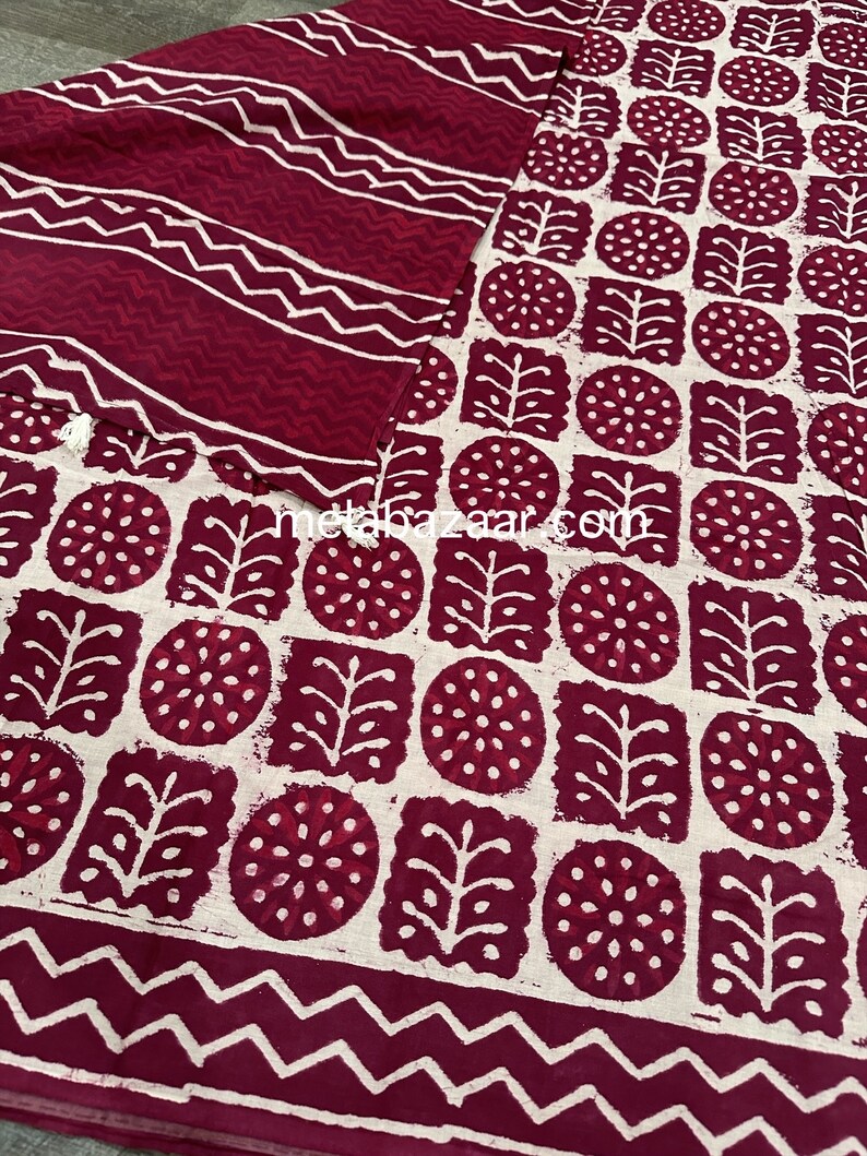 K&ouml;nnte beinhalten: Ein zweiteiliges Set mit einem bordeauxroten und wei&szlig;en geometrischen Muster. Der Stoff zeigt ein sich wiederholendes Design aus Kreisen, Quadraten und Blattformen. Das Set enth&auml;lt ein Oberteil und einen passenden Schal, beide mit wei&szlig;en Zickzack- und Streifenmustern.