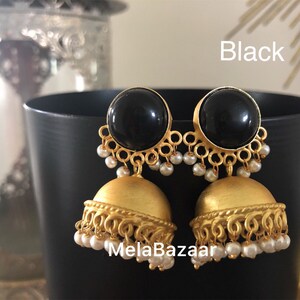 May include: A pair of black and gold-toned earrings. The earrings feature a large, round black stone at the top, with a gold-colored filigree design and small white beads. The bottom portion is a gold-colored bell shape. The word "Black" is visible.