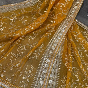 May include: A mustard yellow sheer fabric with a silver embroidered floral pattern and a silver and gold beaded border.