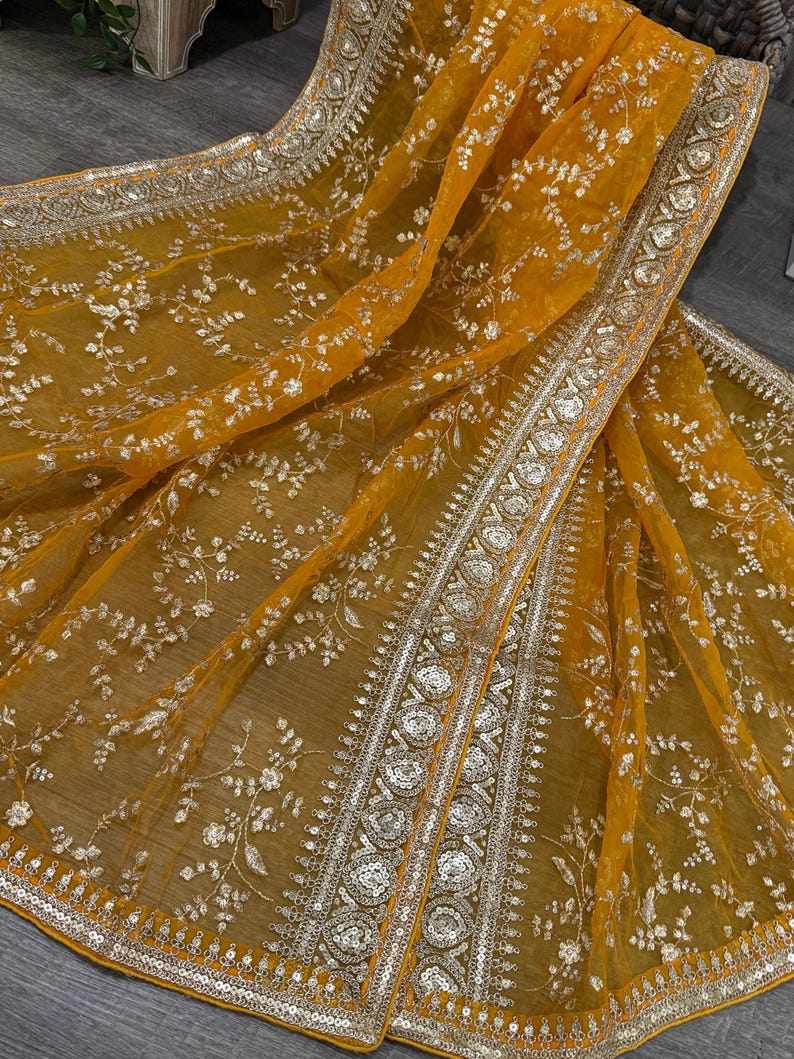 May include: A mustard yellow sheer fabric with a silver embroidered floral pattern and a silver and gold beaded border.