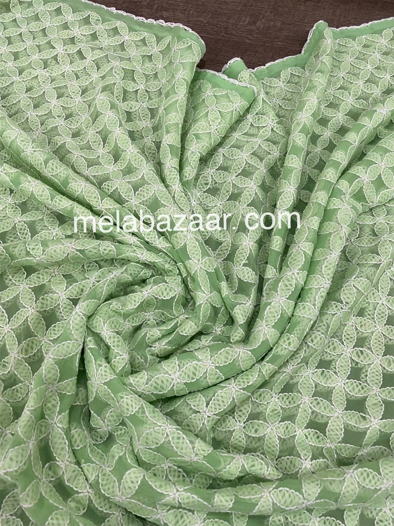 May include: A light green fabric with a white floral embroidery pattern. The fabric is sheer and has a delicate texture.