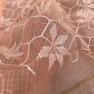 Pode incluir: Um tecido transparente rosa claro com um padr&atilde;o geom&eacute;trico bordado em branco. O tecido &eacute; delicado e tem uma textura macia e fluida.