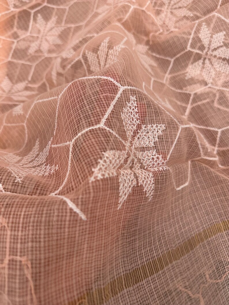 Pode incluir: Um tecido transparente rosa claro com um padr&atilde;o geom&eacute;trico bordado em branco. O tecido &eacute; delicado e tem uma textura macia e fluida.