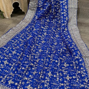 May include: Royal blue fabric with intricate gold floral embroidery. The fabric has a delicate, sheer quality, with a detailed border. The design features small, repeating floral patterns and a decorative edge.