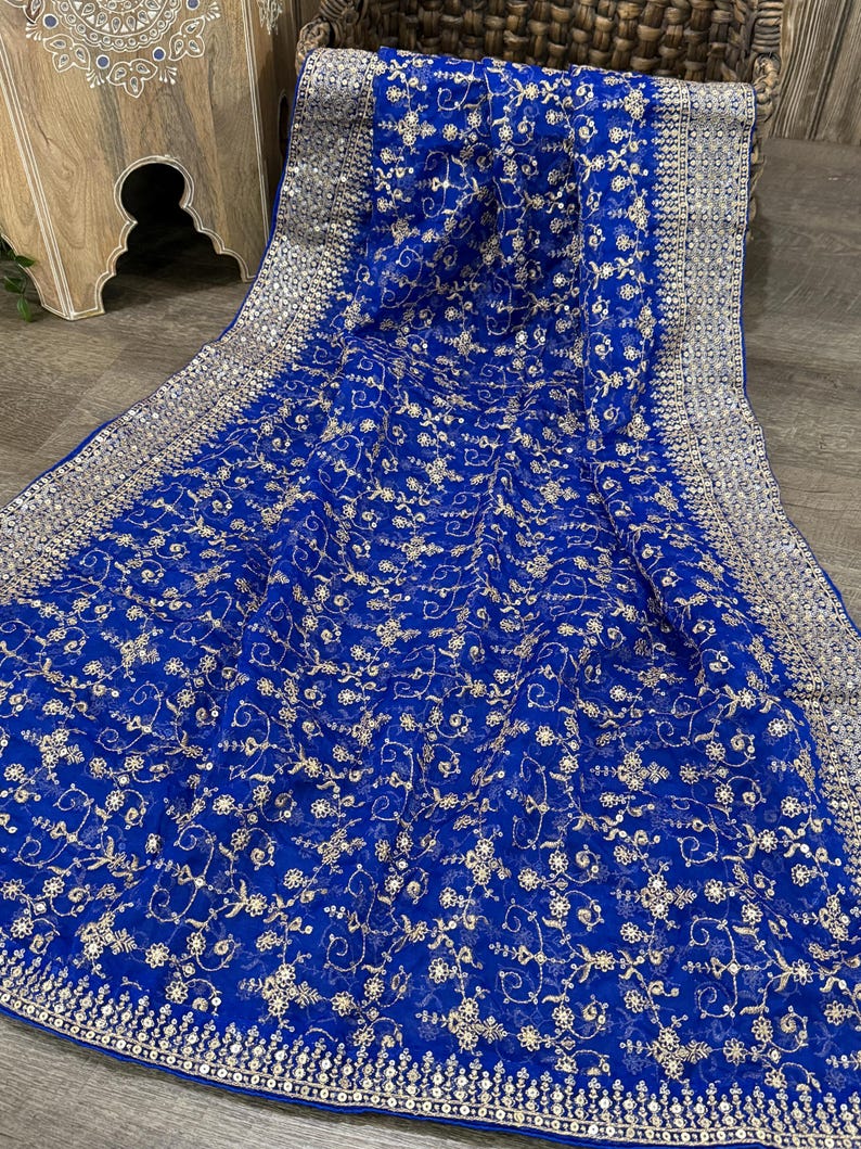 May include: Royal blue fabric with intricate gold floral embroidery. The fabric has a delicate, sheer quality, with a detailed border. The design features small, repeating floral patterns and a decorative edge.