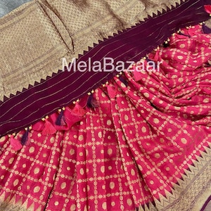Peut inclure: Un sari rose et violet avec une bordure dorée et des glands. Le sari a un motif à carreaux avec de petits motifs floraux. Le texte "Mela Bazaar" est visible sur le sari.