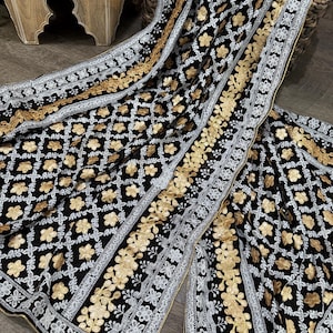 May include: A black sheer shawl with white and gold embroidery. The shawl features a geometric pattern and floral motifs.