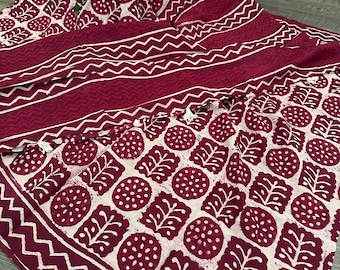Può includere: Tessuto bordeaux e crema con un motivo ripetuto di foglie e cerchi. Il tessuto ha un bordo con un motivo a zig-zag e nappe bianche. Il tessuto è drappeggiato, mostrando il suo design.