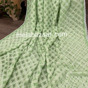 May include: A light green chiffon fabric with white embroidered floral designs. The fabric has a delicate, sheer texture and a subtle sheen.