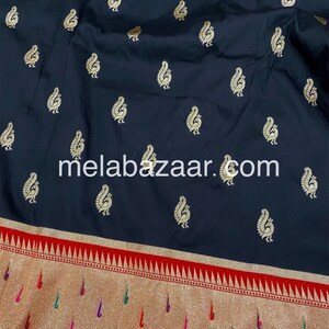 May include: Black silk saree with a gold paisley pattern and a red and gold border. The saree has a website address, "melabazar.com", printed on the fabric.