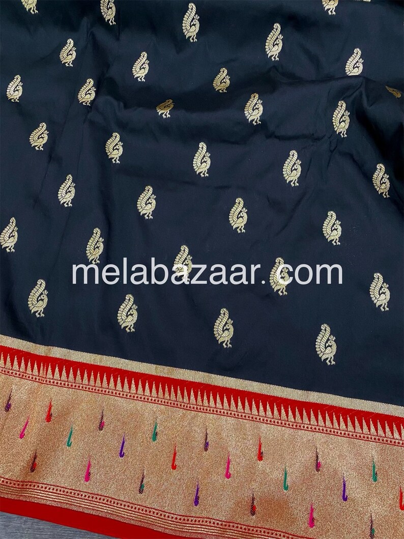 May include: Black silk saree with a gold paisley pattern and a red and gold border. The saree has a website address, "melabazar.com", printed on the fabric.