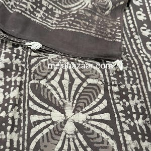 Puede incluir: Una tela de algod&oacute;n marr&oacute;n y blanco con un patr&oacute;n batik. La tela tiene un dise&ntilde;o floral con fondo blanco y detalles marrones. La tela est&aacute; doblada por la mitad y tiene una etiqueta blanca con el texto "melabazaar.com".
