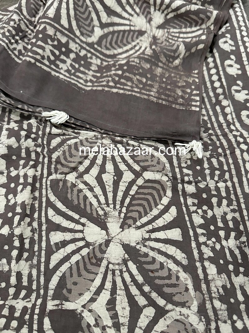 Puede incluir: Una tela de algod&oacute;n marr&oacute;n y blanco con un patr&oacute;n batik. La tela tiene un dise&ntilde;o floral con fondo blanco y detalles marrones. La tela est&aacute; doblada por la mitad y tiene una etiqueta blanca con el texto "melabazaar.com".