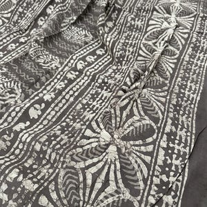 Puede incluir: Tela gris con un patr&oacute;n batik blanco de flores, hojas y formas geom&eacute;tricas.