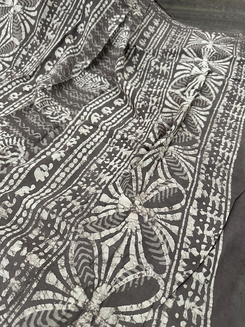Puede incluir: Tela gris con un patr&oacute;n batik blanco de flores, hojas y formas geom&eacute;tricas.