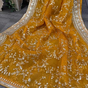 May include: A mustard yellow sheer fabric with silver embroidery. The fabric has a floral pattern and a silver border with sequins.