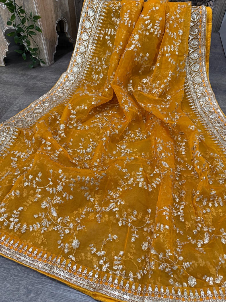 May include: A mustard yellow sheer fabric with silver embroidery. The fabric has a floral pattern and a silver border with sequins.