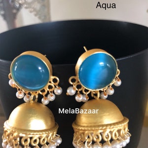 May include: Gold-toned earrings with a round, aqua-colored stone top and a bell-shaped bottom. The earrings are adorned with small, dangling white pearls. The word "Aqua" is visible in the image.