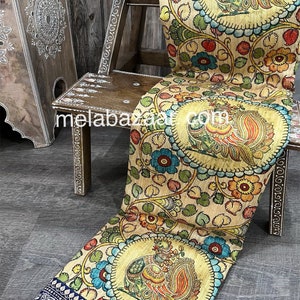 May include: A beige silk saree with a blue border and a colorful hand-painted design featuring peacocks and floral motifs.