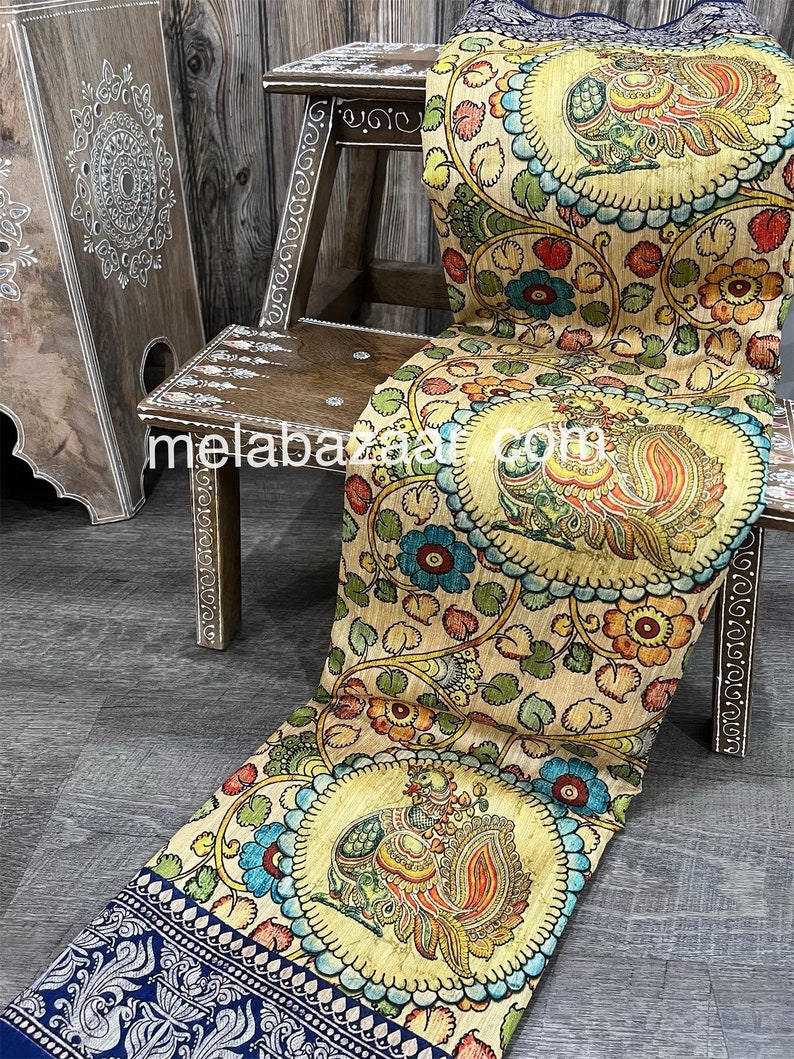 May include: A beige silk saree with a blue border and a colorful hand-painted design featuring peacocks and floral motifs.