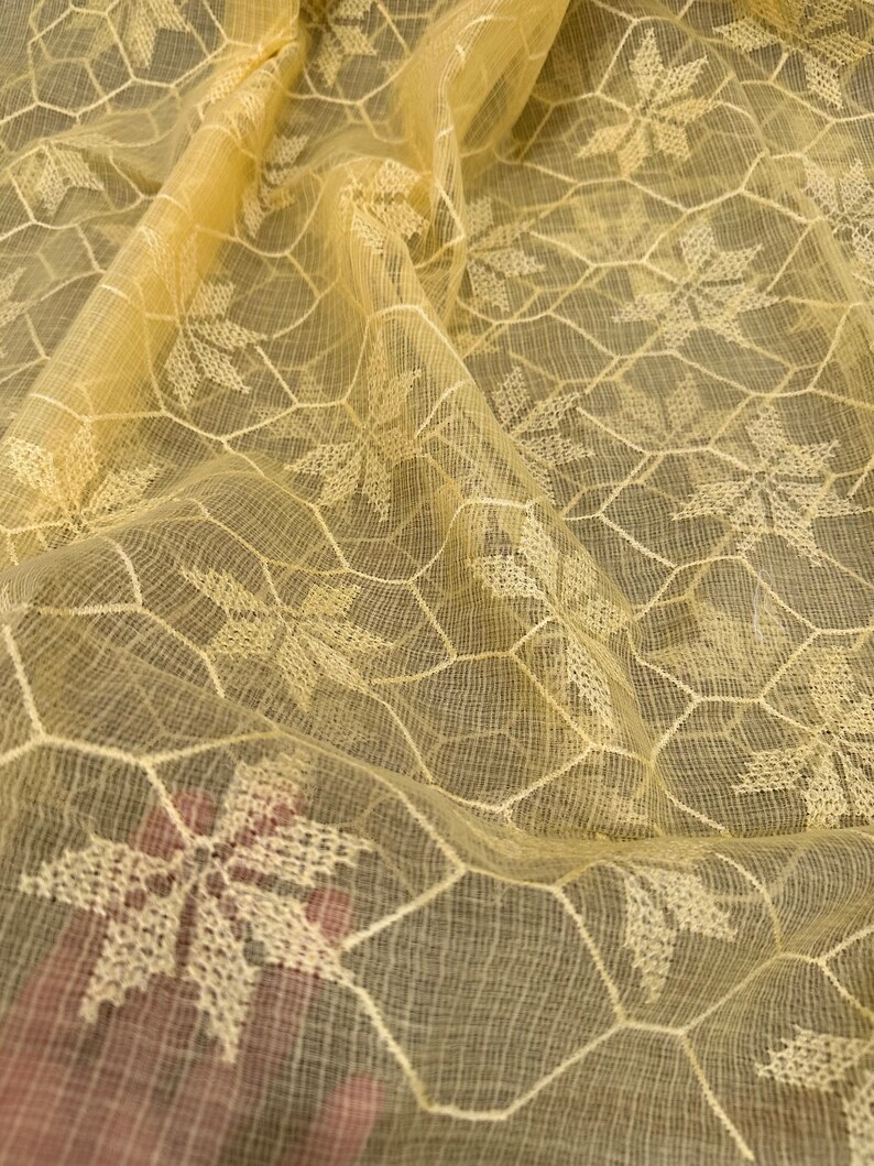 Pode incluir: Tecido transparente amarelo claro com um delicado padr&atilde;o floral branco. O tecido tem uma textura de favo de mel e &eacute; perfeito para projetos de artesanato ou costura.