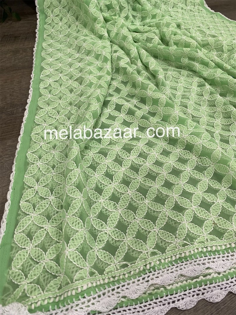 May include: A light green sheer fabric with a white embroidered floral pattern. The fabric has a white crocheted trim around the edges. The text "melabazar.com" is visible in the center of the image.