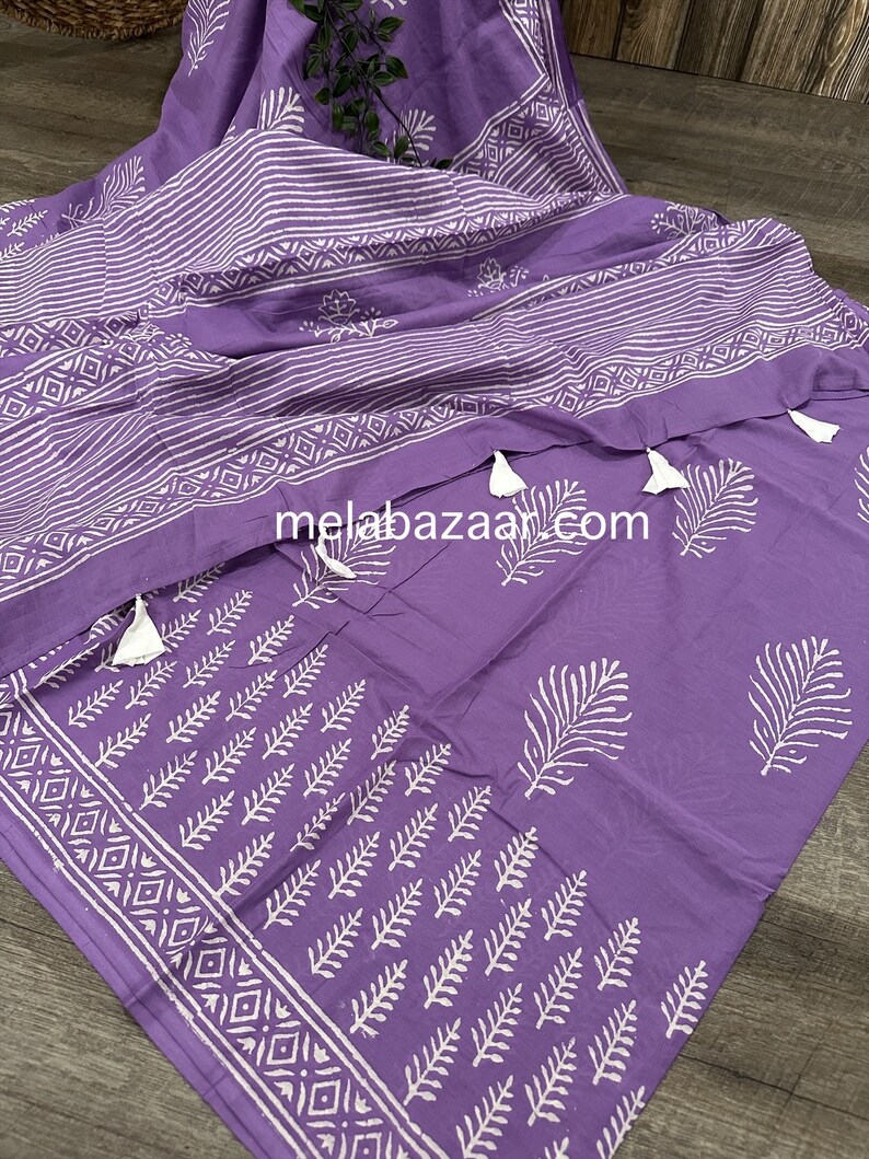 May include: Purple cotton fabric with white block printed designs of leaves and geometric patterns. The fabric has tassels on the edges.