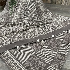 Puede incluir: Una tela de algod&oacute;n gris con un dise&ntilde;o de estampado en bloque blanco. La tela presenta una variedad de patrones geom&eacute;tricos, incluyendo rayas, cuadrados y motivos florales.