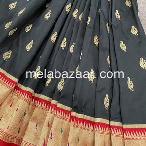 May include: Black silk saree with a gold peacock design and a red and gold border. The saree is folded and the border is visible. The saree is a traditional Indian garment.