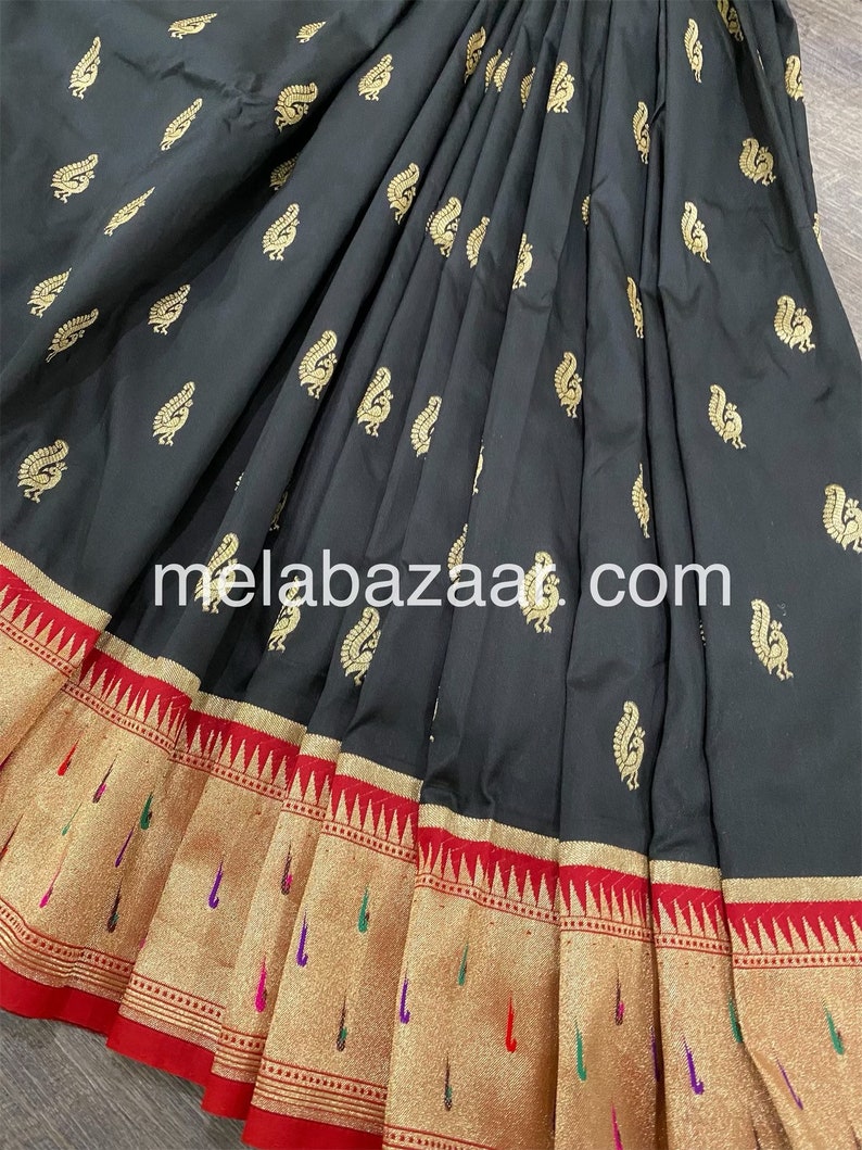 May include: Black silk saree with a gold peacock design and a red and gold border. The saree is folded and the border is visible. The saree is a traditional Indian garment.