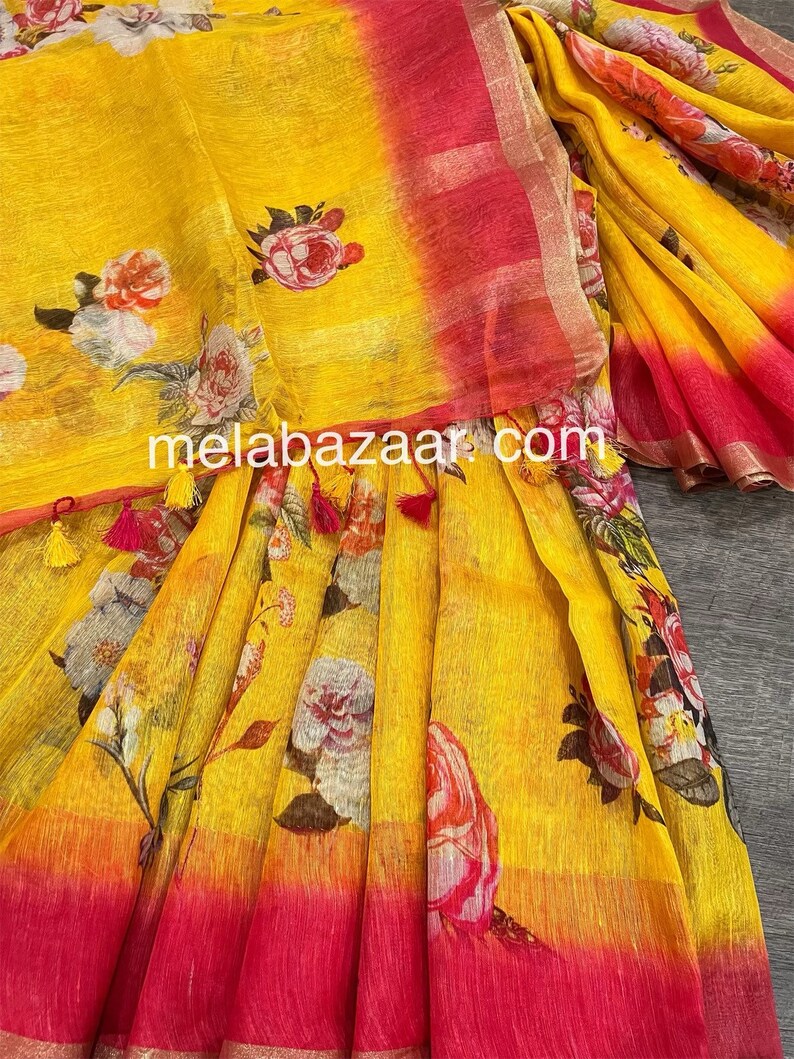 May include: Yellow linen saree with a pink border and floral print. The saree has a gradient effect with a darker yellow at the top and a lighter yellow at the bottom. The floral print is in shades of pink, white, and green.
