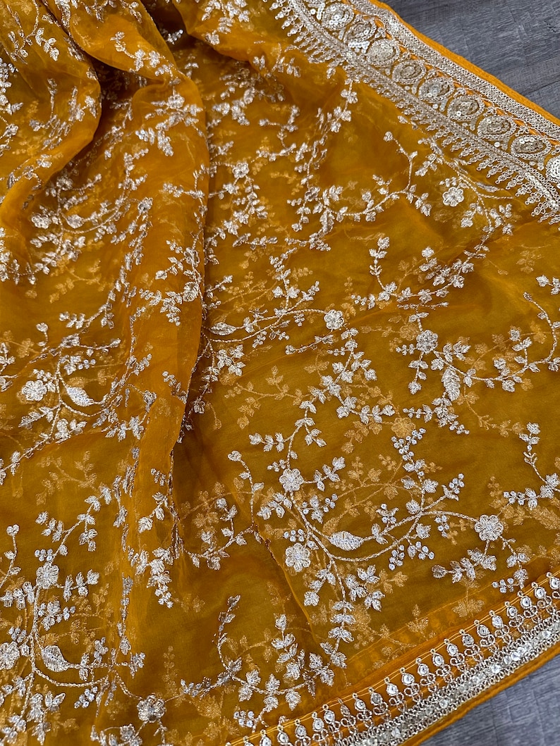 May include: A mustard yellow sheer fabric with a silver floral embroidery pattern. The fabric has a silver beaded border.